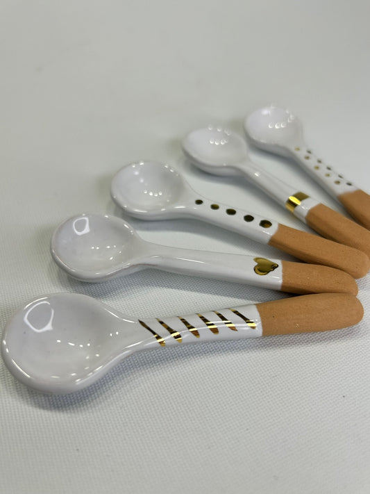 Cinque cucchiai bianchi con il manico di terracotta grezza, accostati su fondo chiaro.