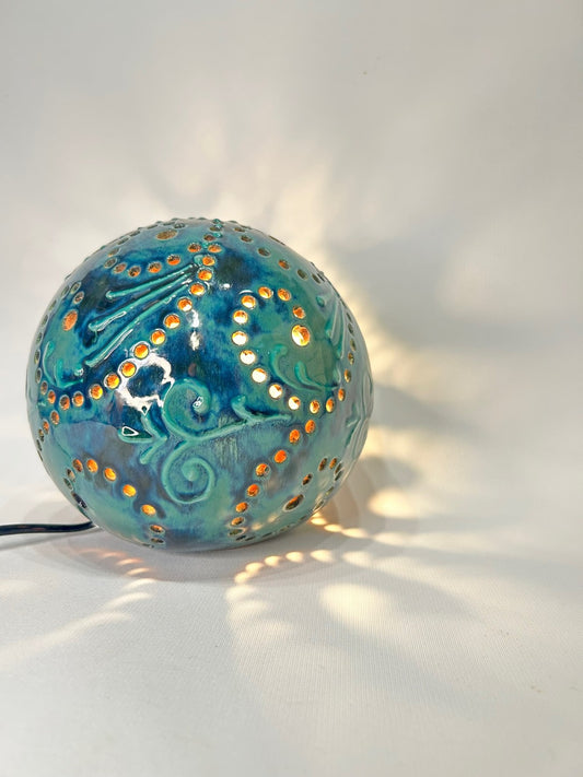 La sfera accesa su un piano chiaro: i fori proiettano punti di luce tutto intorno.