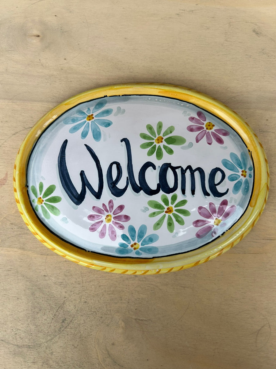 Targa ovale con «Welcome» e margherite colorate, bordo giallo a treccia.