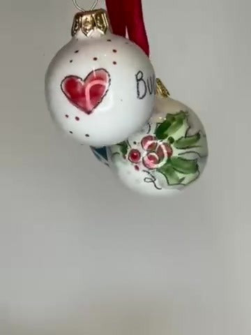 Due palline in primo piano, con il cuore rosso e le foglie di agrifoglio.