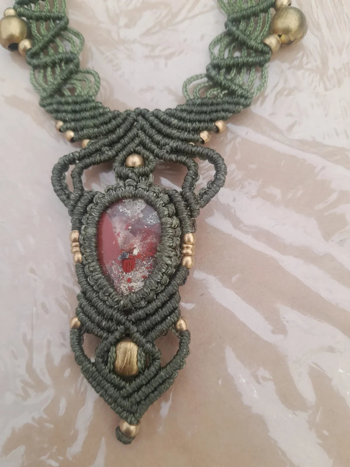 La collana da vicino: il filo verde oliva annodato fitto, le perle di metallo brunito e la pietra rossa a goccia al centro
