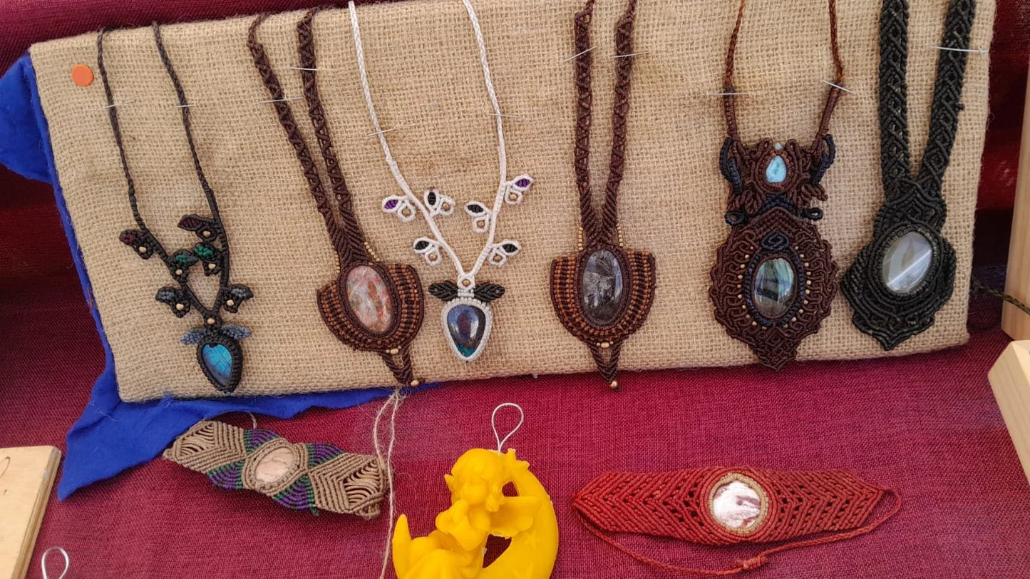 Pendenti in macramè nero e marrone con le pietre chiare appesi sulla juta, e sotto due bracciali a fascia con la pietra al centro