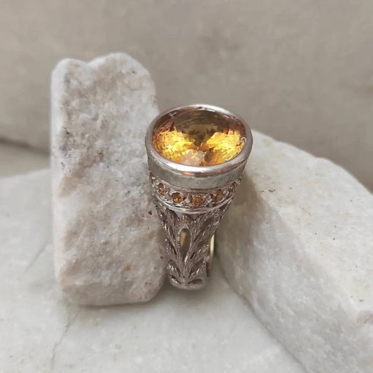L'anello in piedi su una pietra chiara: il castone alto, la fila di citrini piccoli e il traforo del gambo