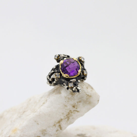 L'anello di tre quarti sulla pietra bianca: l'ametista a scacchiera nel castone d'oro giallo e il corpo d'argento brunito aperto a vuoti irregolari.