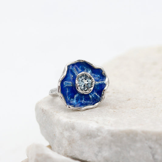 L'anello su una lastra di pietra chiara, la corolla vista di fronte con lo smalto blu e il topazio al centro
