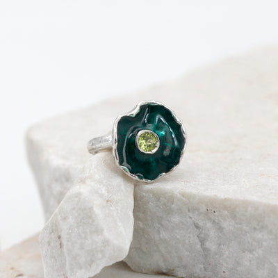 La corolla vista quasi dall'alto: smalto verde scuro dentro il bordo d'argento ondulato, peridoto tondo al centro
