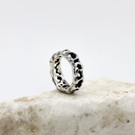 L'anello di tre quarti sul bordo di una pietra chiara: la fascia stretta, bucata per tutto il giro.