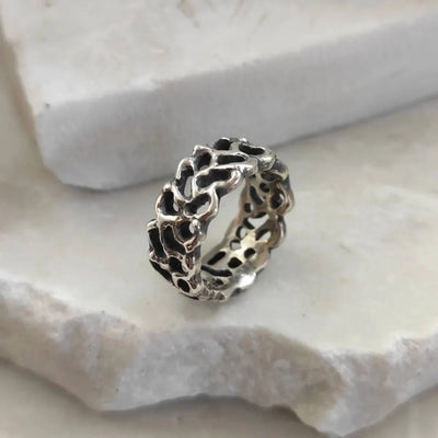 The ring in three-quarter view, resting on the edge of a light stone: the silver mesh and the openings that break it up.
