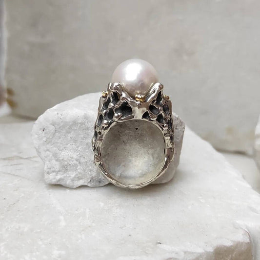 L'anello visto di fronte: la perla bianca in cima, le quattro braccia d'argento che la trattengono e la fascia forata sotto