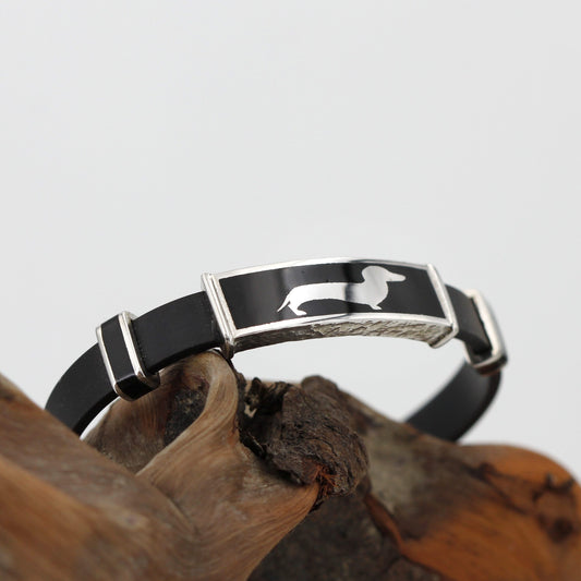 Il bracciale inarcato sopra un legno scuro, con la targhetta del bassotto in alto