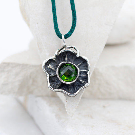Il fiore d'argento appoggiato a una pietra bianca, con lo zircone verde al centro della corolla