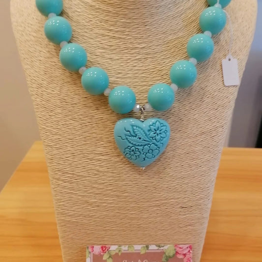Collana di grandi sfere turchesi con pendente a cuore inciso a fiori e farfalla, su espositore