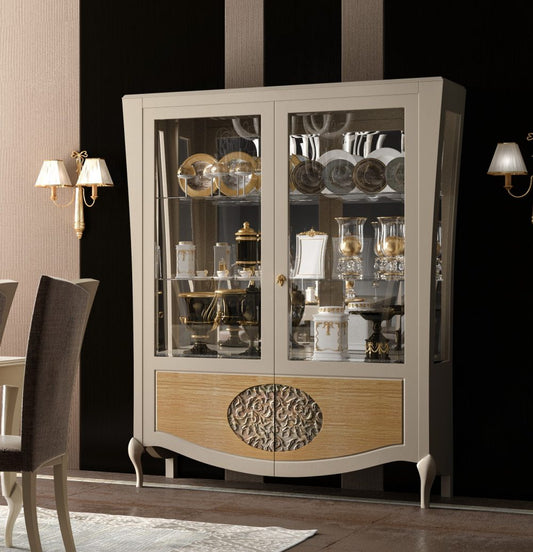 La vetrina 862 illuminata: le due ante a vetro, la fascia bassa in rovere naturale e l'ovale intagliato in argento