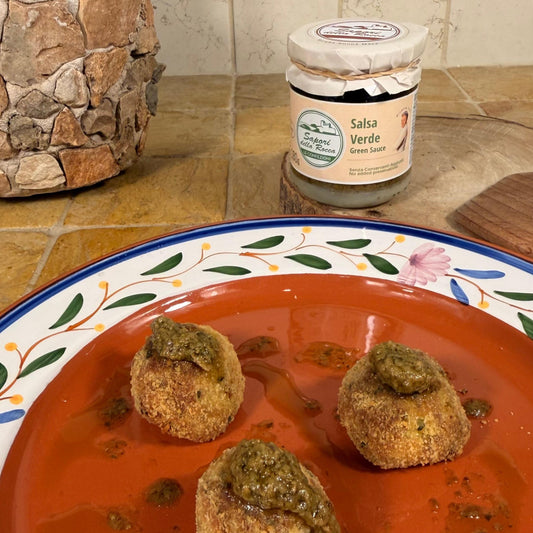 Tre polpette panate in un piatto decorato, con la salsa verde sopra e il vasetto dietro