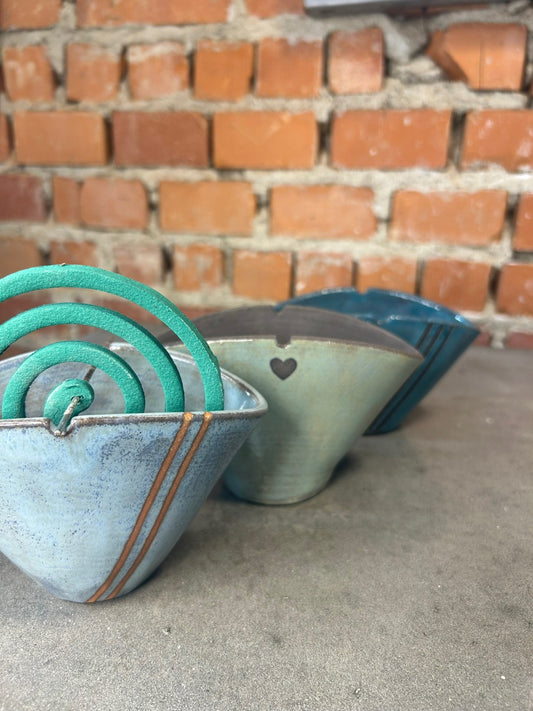 Tre pezzi di ceramica azzurra allineati contro un muro di mattoni, con la spirale verde già inserita.