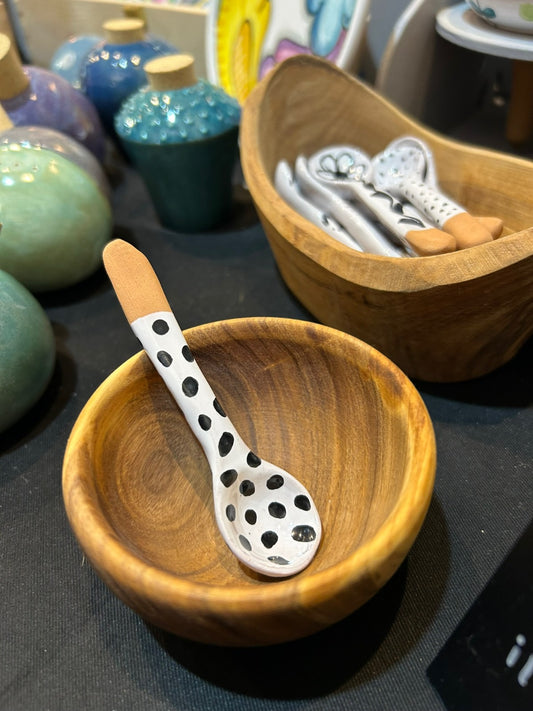 Un cucchiaio bianco a pois neri appoggiato dentro una ciotola di legno.