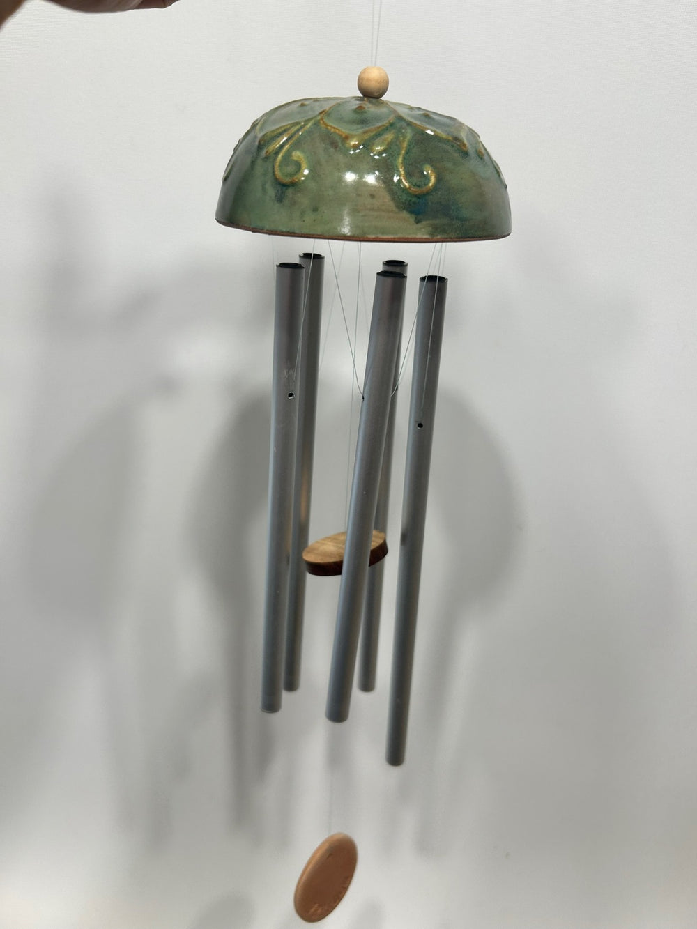 La calotta verde appesa a una parete chiara, con le canne di metallo e il battaglio di legno.