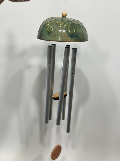 La calotta verde appesa a una parete chiara, con le canne di metallo e il battaglio di legno.