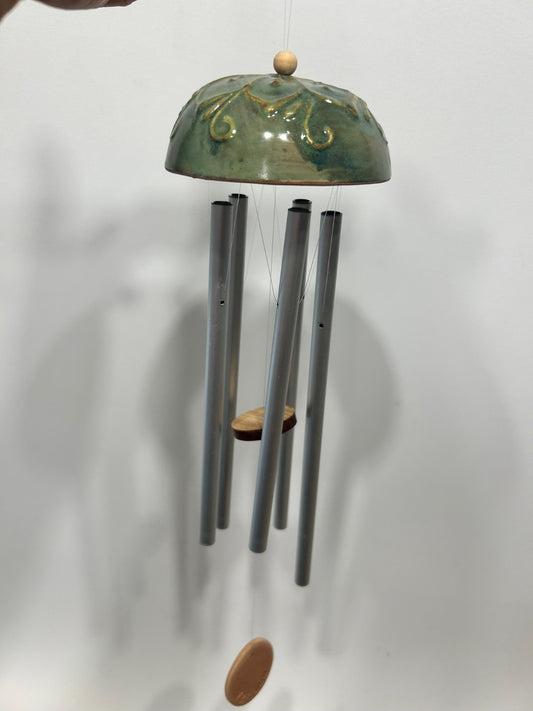 La calotta verde appesa a una parete chiara, con le canne di metallo e il battaglio di legno.