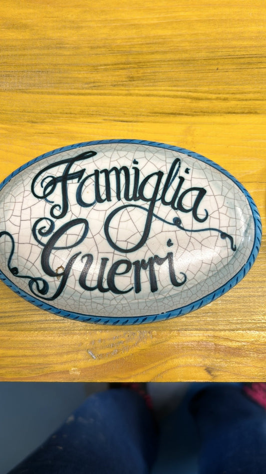 Targa ovale con la scritta «Famiglia Guerri» su fondo bianco screziato e bordo blu.