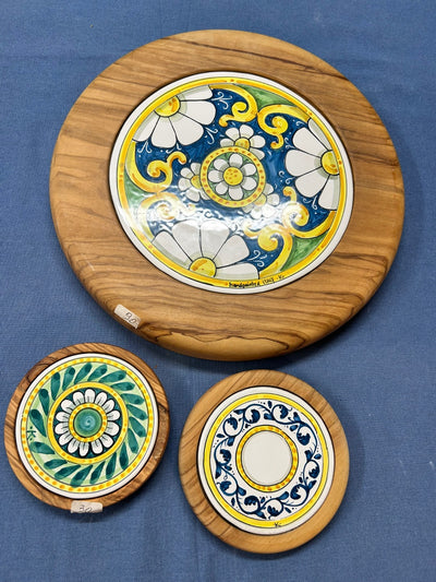 Tre supporti di legno con la ceramica dipinta incastonata, uno grande e due piccoli, su un telo blu.