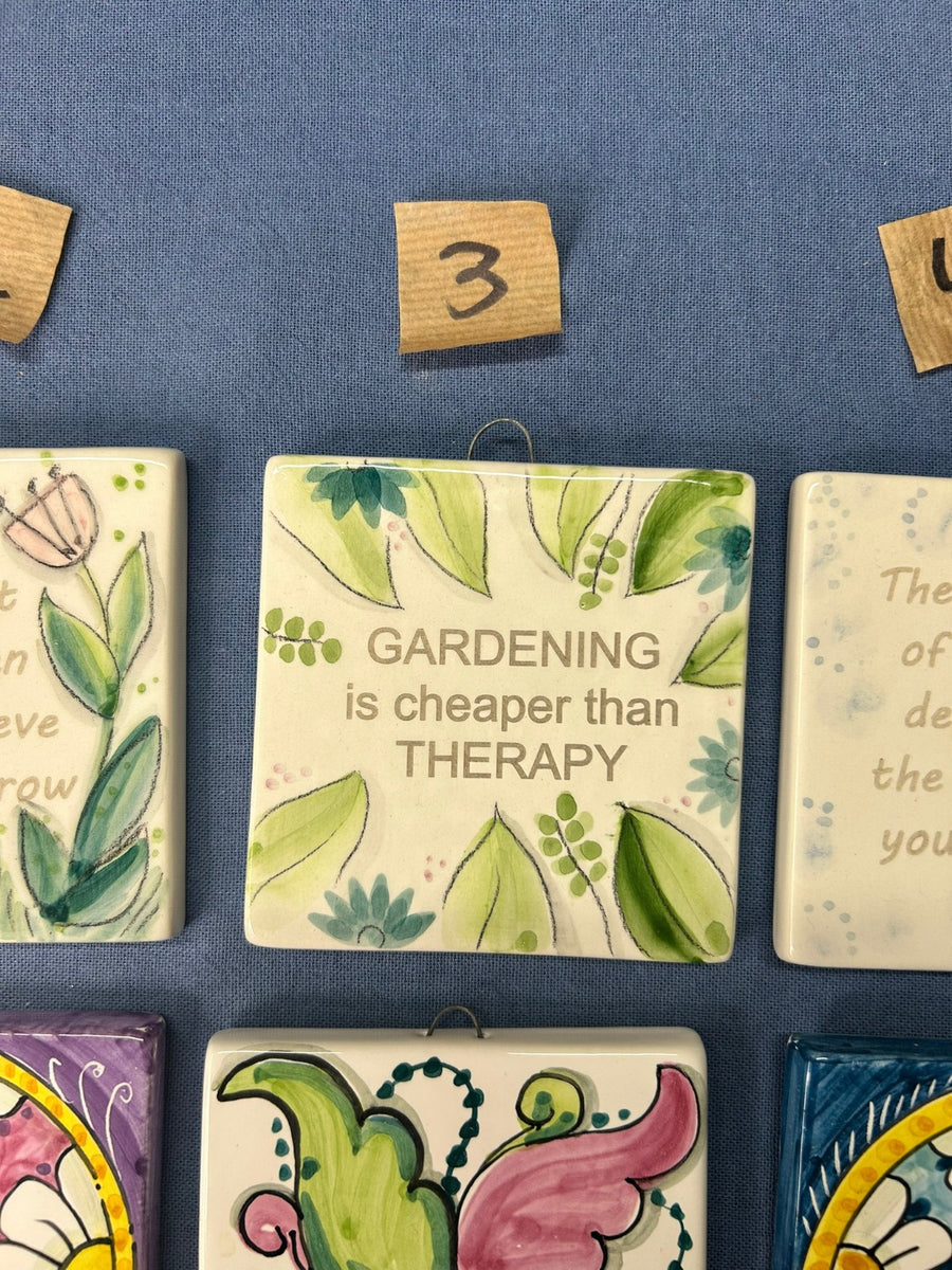 La mattonella con le foglie verdi e la frase «Gardening is cheaper than therapy».
