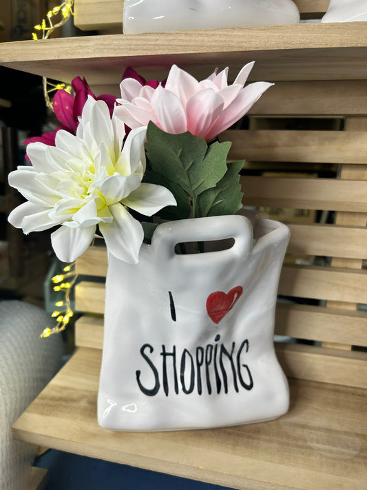Una borsetta bianca con «I love shopping» piena di fiori bianchi e rosa.
