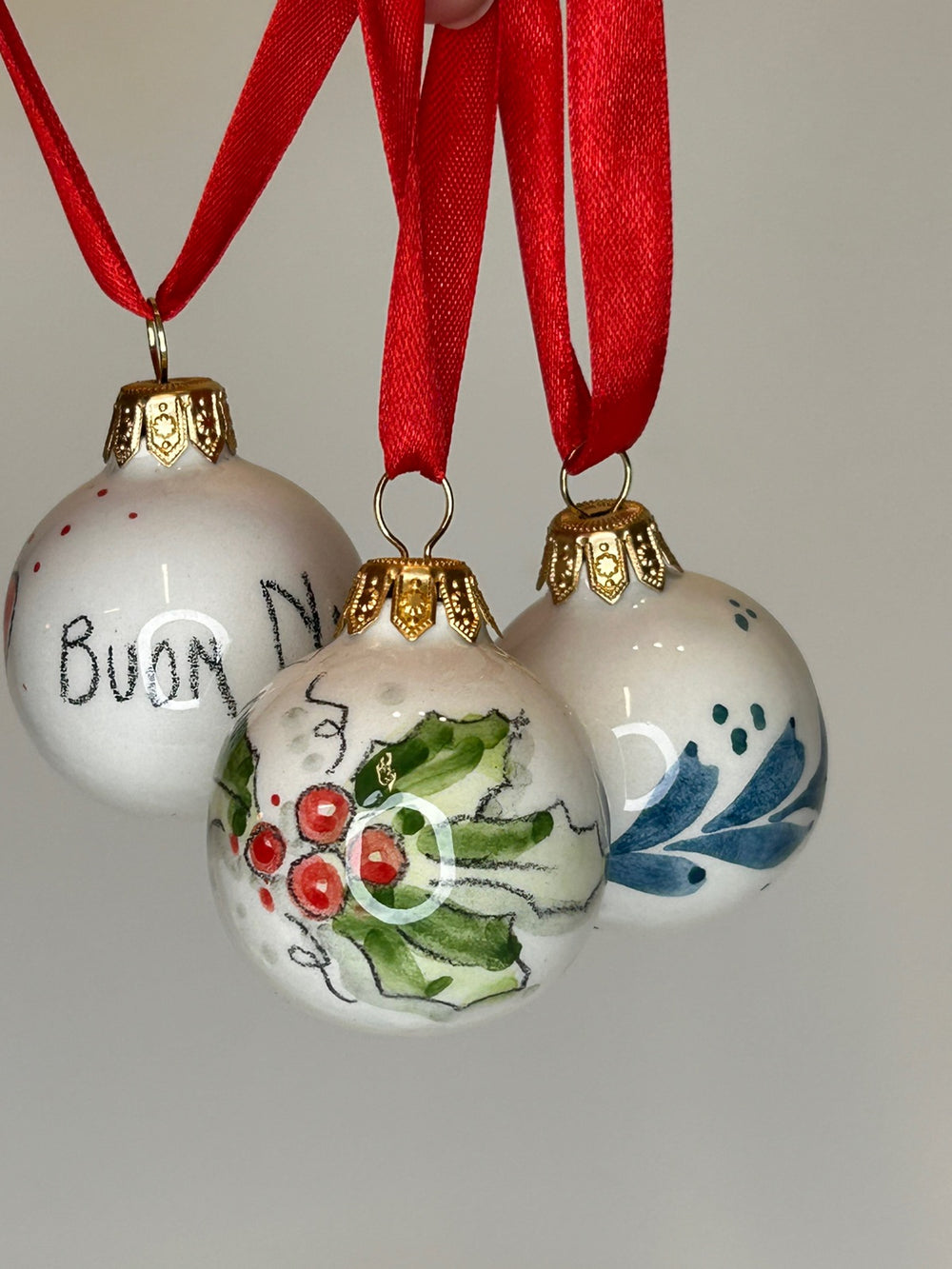 Quattro palline appese ai nastri rossi, con agrifoglio, cuori e la scritta «Buon Natale».