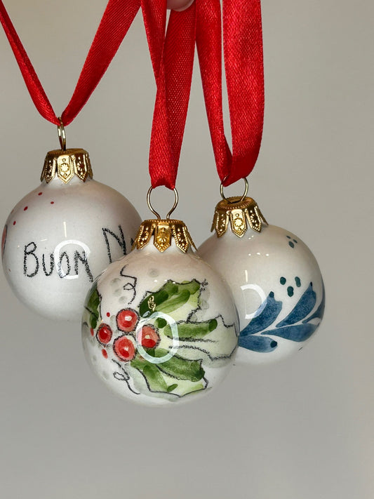 Quattro palline appese ai nastri rossi, con agrifoglio, cuori e la scritta «Buon Natale».