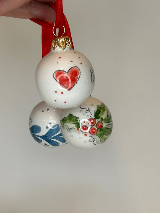 Tre palline tenute per il nastro: il cuore rosso, le bacche e il tralcio blu.