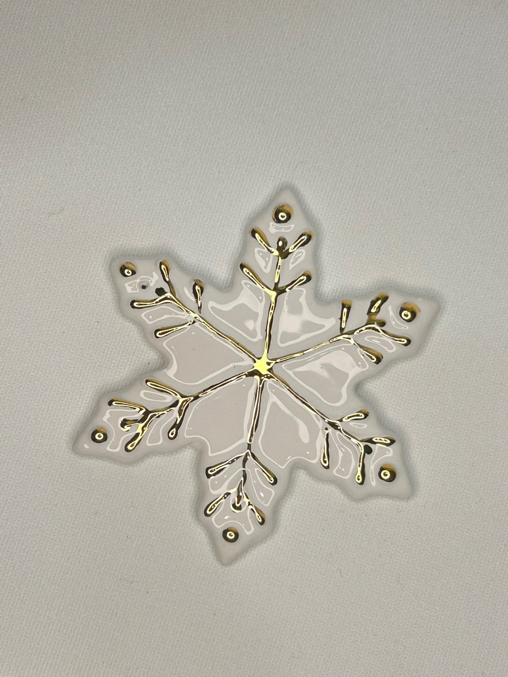 Un fiocco di neve bianco con i rametti e i puntini dipinti in oro.