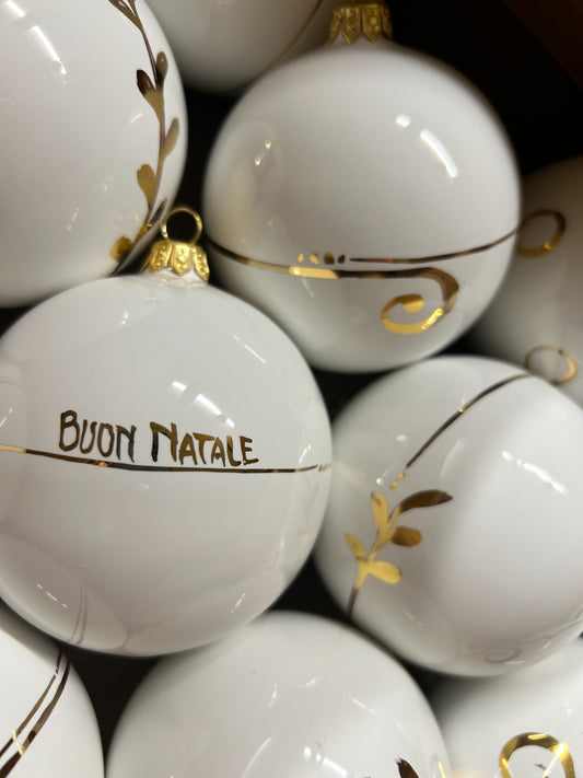 Sfere bianche lucide ammucchiate, una con la scritta «Buon Natale» e i tralci dorati.