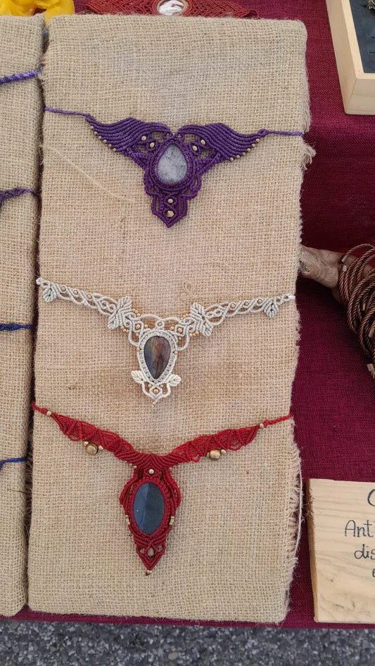 Tre collari in macramè sulla juta: viola, bianco e rosso, ognuno con la pietra al centro