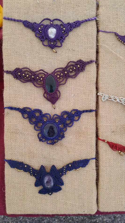 Quattro collari in macramè viola e blu con le pietre al centro, appesi sulla juta