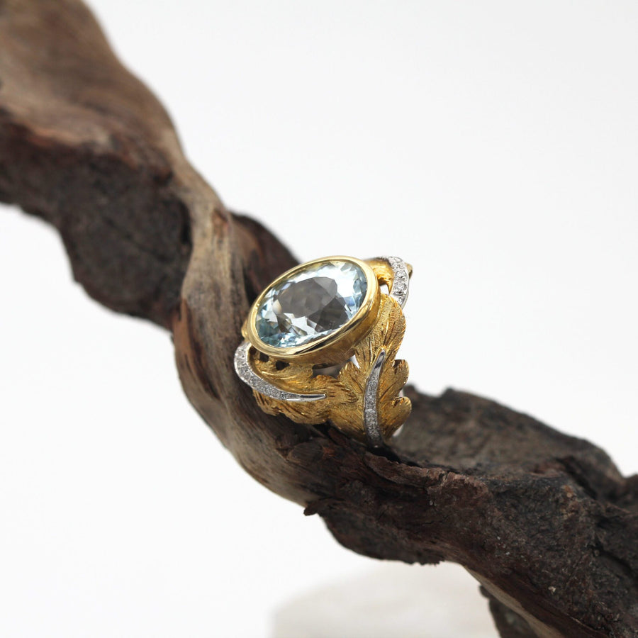 The ring resting on a dry branch, three-quarter view: the yellow gold against the dark bark