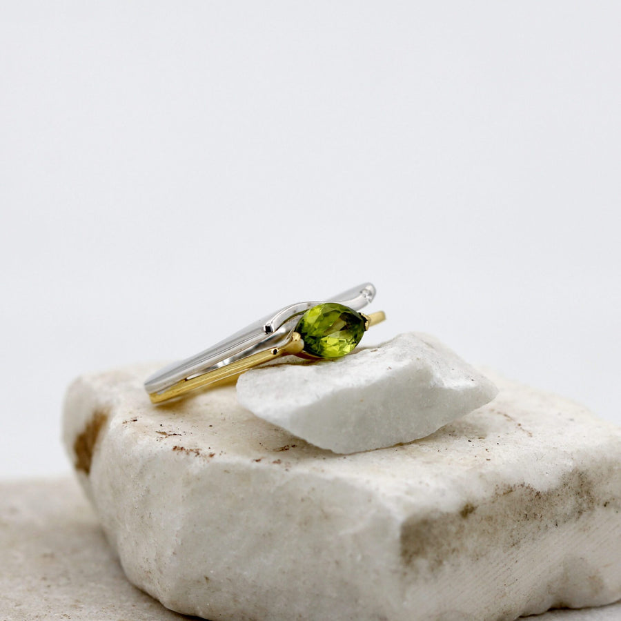 The ring resting on its side, with the peridot held by the yellow gold prongs
