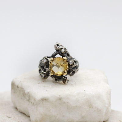 The ring from the front: at the centre the checkerboard citrine quartz in the yellow gold bezel, around it the burnished silver pierced with craters and the grey diamonds.