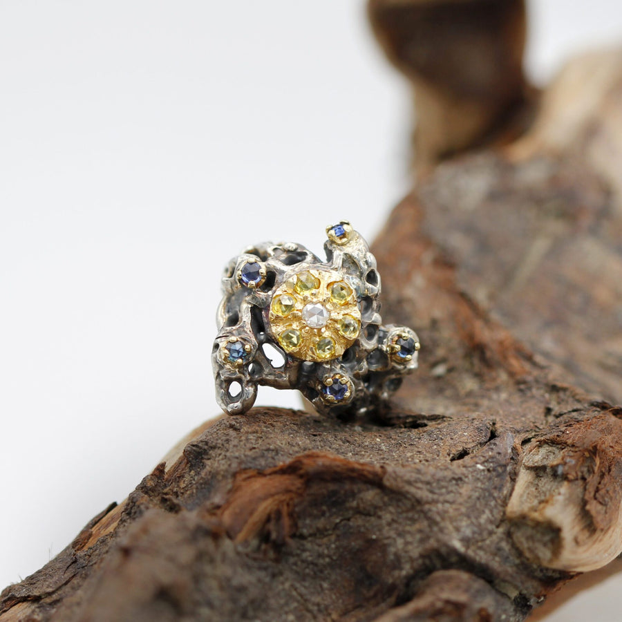 The ring resting on a piece of wood, in three-quarter view, with the gold disc turned to the left