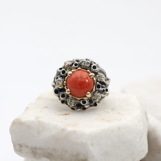 L'anello visto dall'alto: il corallo tondo nel castone d'oro e i sei diamanti grigi intorno