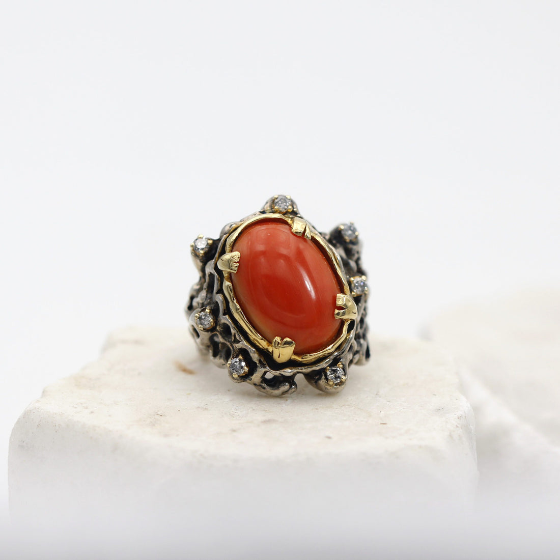 Il corallo cabochon nel castone in oro, con i sette diamanti grigi intorno