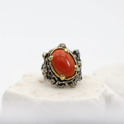 Il corallo cabochon nel castone in oro, con i sette diamanti grigi intorno