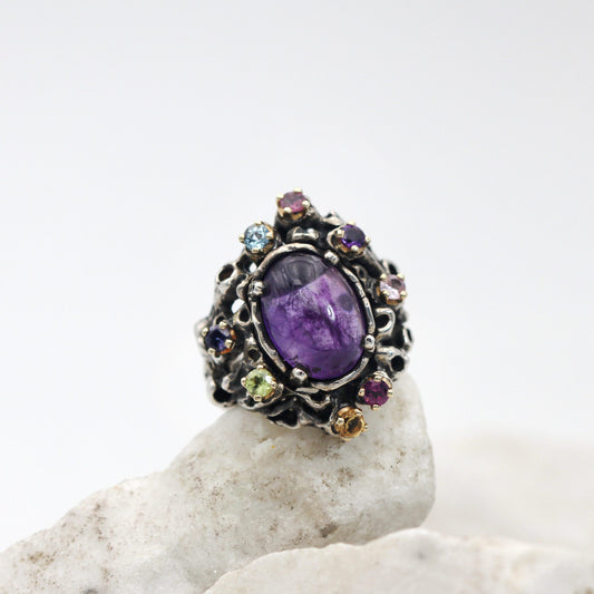 L'anello di fronte: l'ametista ovale a cabochon nel castone d'argento e le otto pietre di colore su griffe d'oro tutt'intorno