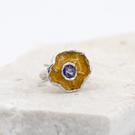 L'anello in piedi su una lastra di pietra chiara, la corolla vista di fronte con lo smalto giallo dentro e la iolite al centro
