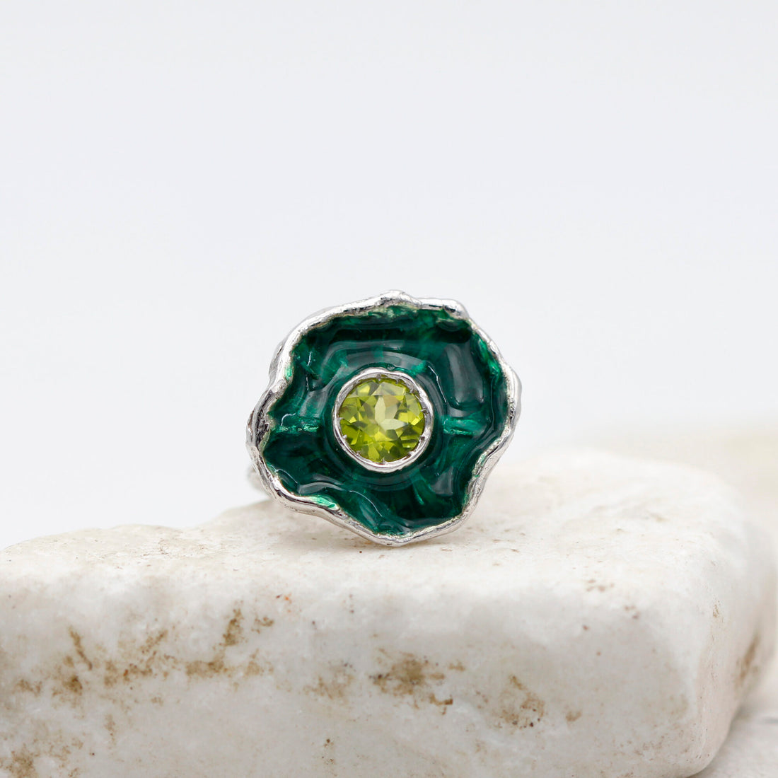 L'anello su una lastra di pietra chiara, la corolla vista di fronte con lo smalto verde dentro e il peridoto al centro