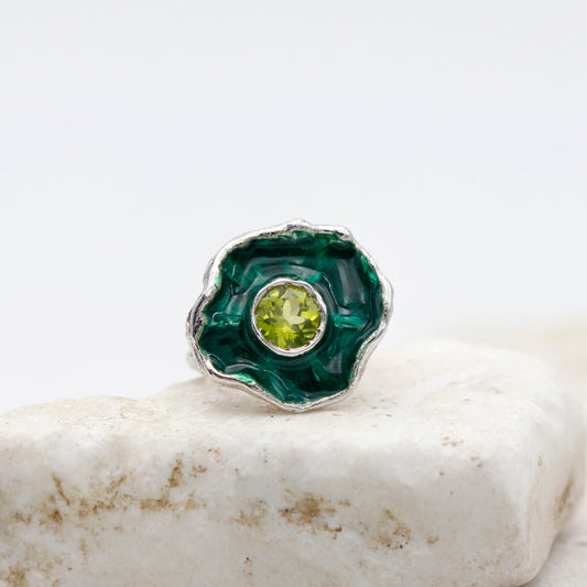 L'anello su una lastra di pietra chiara, la corolla vista di fronte con lo smalto verde dentro e il peridoto al centro