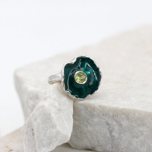 La corolla vista quasi dall'alto: smalto verde scuro dentro il bordo d'argento ondulato, peridoto tondo al centro