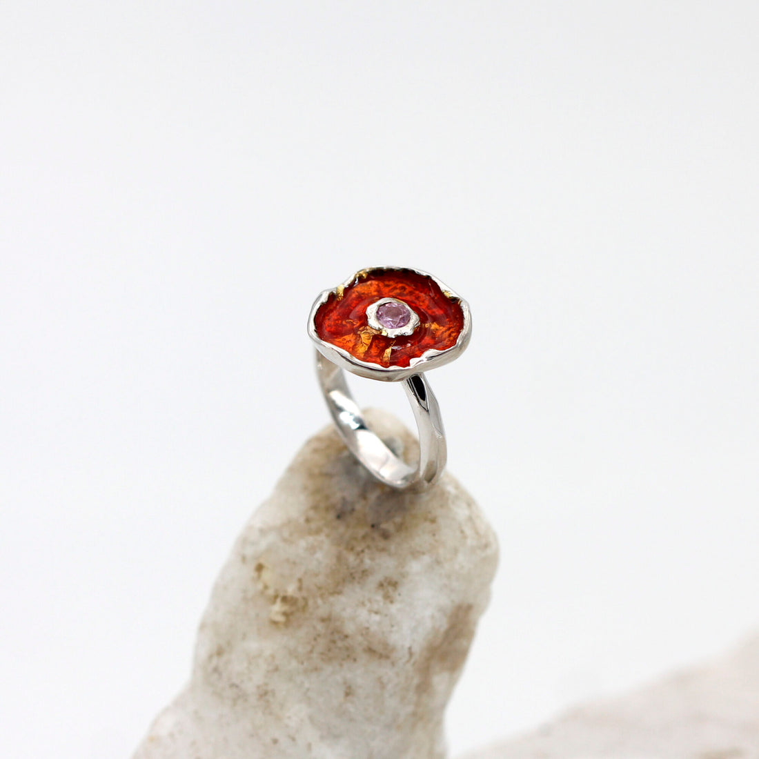 L'anello in equilibrio su un sasso chiaro: la corolla rosso rame con il quarzo rosa al centro