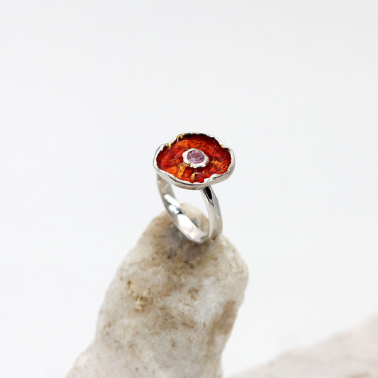 L'anello in equilibrio su un sasso chiaro: la corolla rosso rame con il quarzo rosa al centro