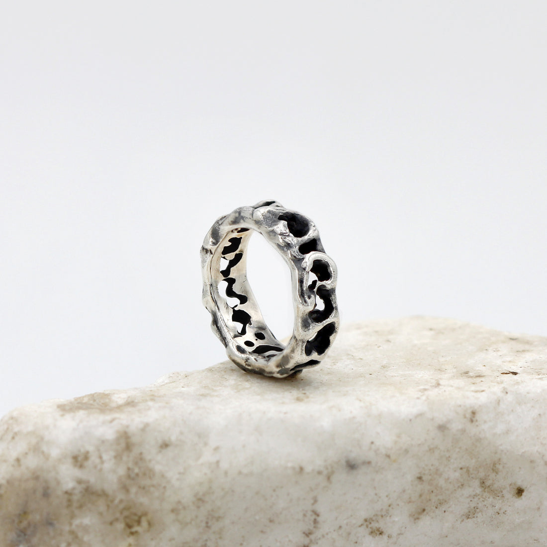 L'anello di tre quarti sul bordo di una pietra chiara: la fascia stretta, bucata per tutto il giro.