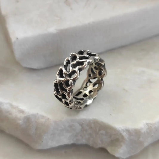L'anello di tre quarti, appoggiato al bordo di una pietra chiara: la maglia d'argento e i vuoti che la aprono.